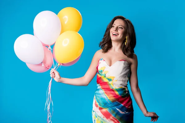 Happy elegant young woman in dress holding balloons isolated on blue — Stock Photo