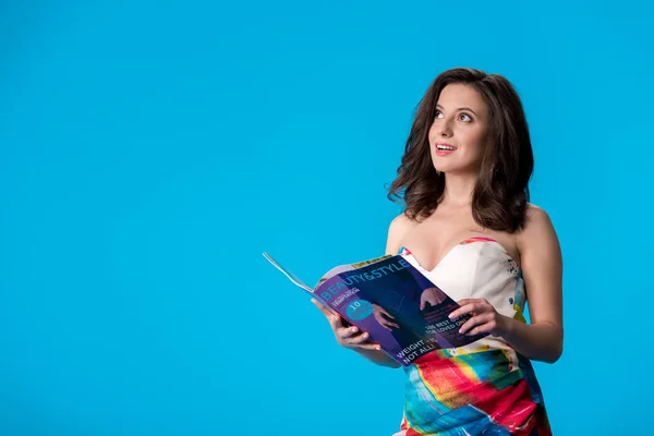 Mujer joven elegante de ensueño en vestido con estilo de celebración y la revista de belleza aislado en azul - foto de stock