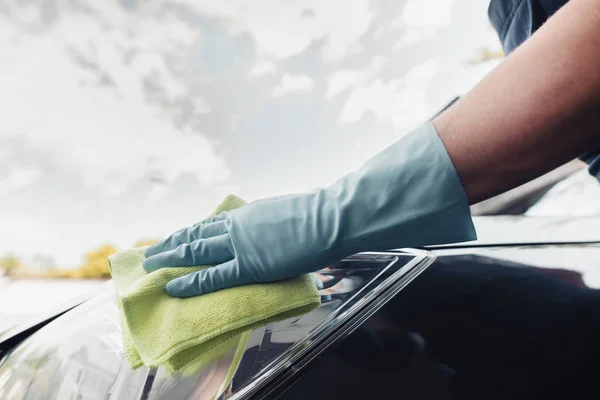 Vue recadrée du nettoyeur de voiture dans le gant en caoutchouc essuyant voiture avec chiffon — Photo de stock