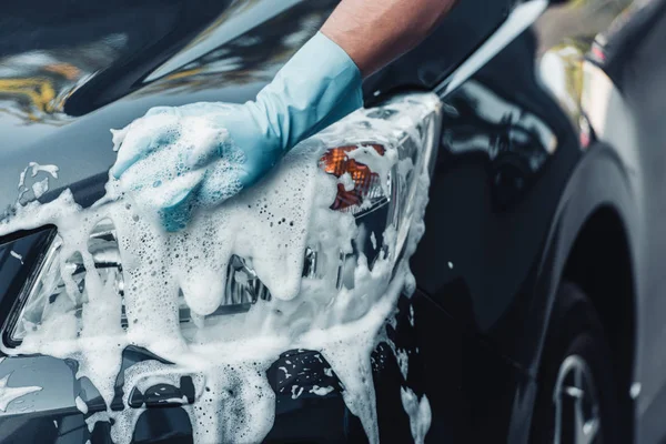 Vue partielle du lave-auto nettoyant voiture avec éponge et détergent — Photo de stock