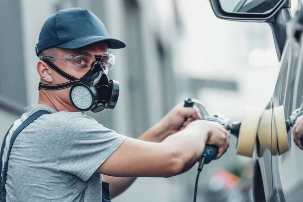 Young car cleaner in respirator and protective glasses polishing car with polish machine — Stock Photo