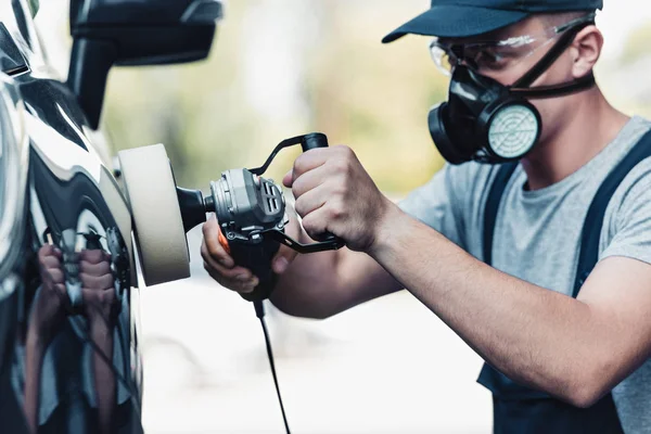 Car cleaner in respirator and protective glasses polishing car with polish machine — Stock Photo