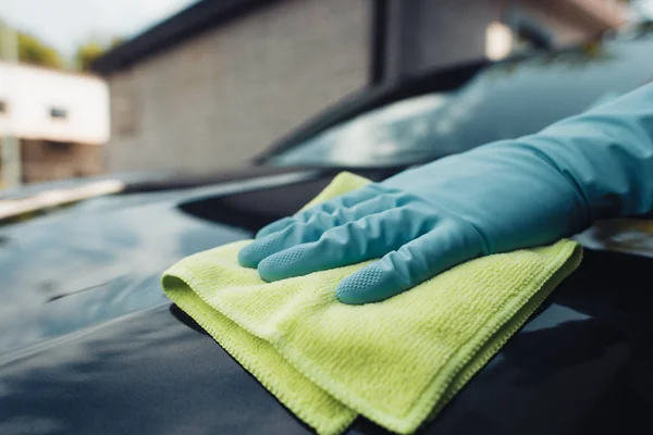Обрезанный вид автомойки в резиновых перчатках вытирая автомобиль тряпкой — стоковое фото