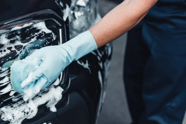 Vue recadrée du nettoyeur de voiture lavage lampe arrière avec éponge et détergent — Photo de stock