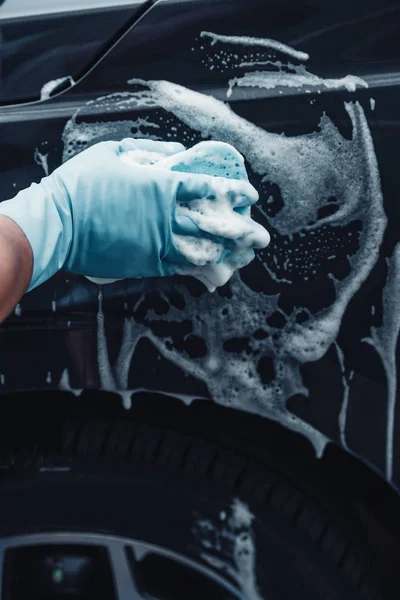 Partial view of car cleaner washing black car with sponge and detergent — Stock Photo