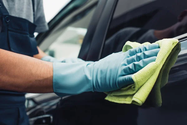 Ausgeschnittene Ansicht von Autoputzer wischt schwarzes Auto mit Lappen ab — Stockfoto