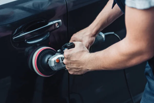 Partial view of car cleaner polishing black car door with buffer machine — Stock Photo