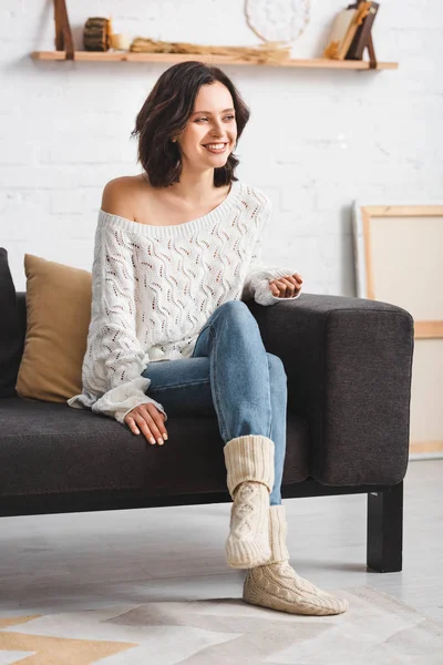 Femme brune heureuse assise sur un canapé dans un salon confortable — Photo de stock