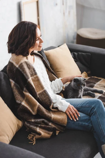 Jolie femme dans la couverture assis sur le canapé avec chat — Photo de stock