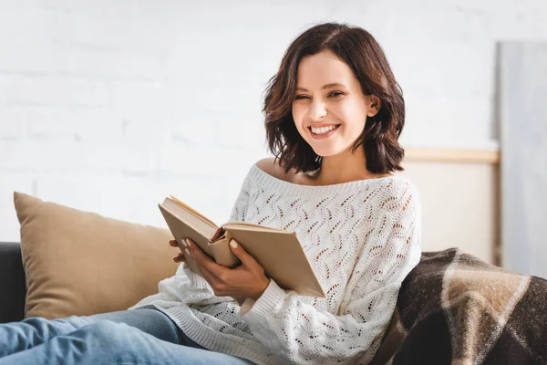 Menina alegre leitura livro no sofá em casa — Fotografia de Stock