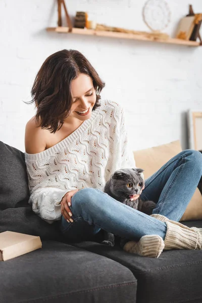 Счастливая молодая женщина, сидящая на диване со складным котом — стоковое фото