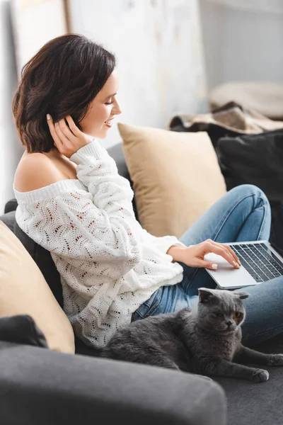 Bela mulher sorridente usando laptop com escocês gato dobra no sofá — Fotografia de Stock