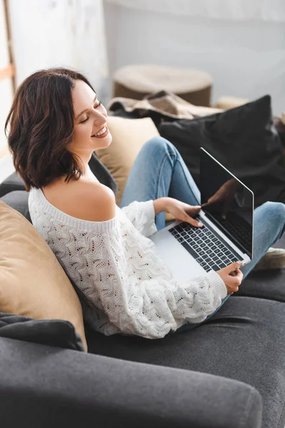 Belle fille heureuse en utilisant un ordinateur portable sur le canapé dans le salon confortable — Photo de stock