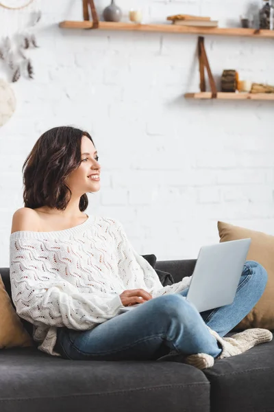 Красивая улыбающаяся девушка с ноутбуком на диване в уютной гостиной — стоковое фото