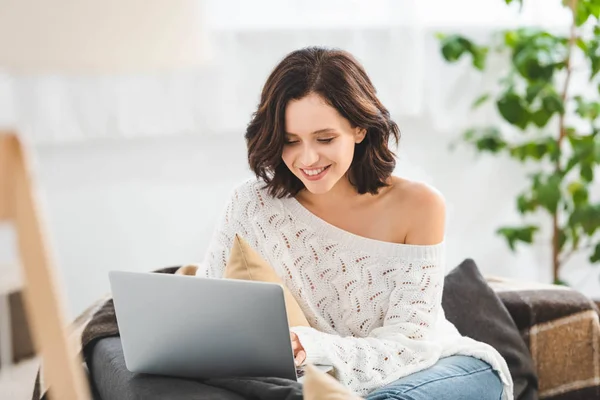 Attractive cheerful girl using laptop on sofa in cozy living room — Stock Photo