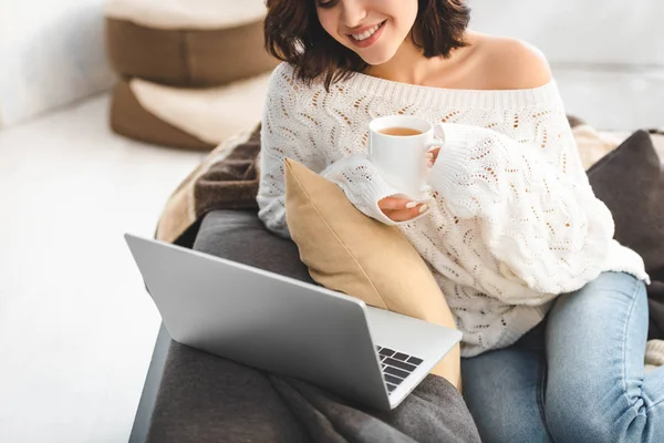 Привлекательная девушка с чашкой чая с помощью ноутбука в уютном доме — стоковое фото