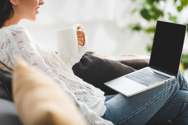 Vista recortada de chica con taza de café viendo la película en el ordenador portátil con pantalla en blanco - foto de stock