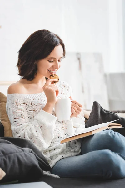 Glückliches Mädchen liest Buch auf Sofa mit Kaffee und Keksen — Stockfoto