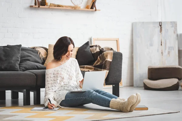 Chica sonriente con auriculares estudiando en línea con el ordenador portátil y portátil en casa - foto de stock