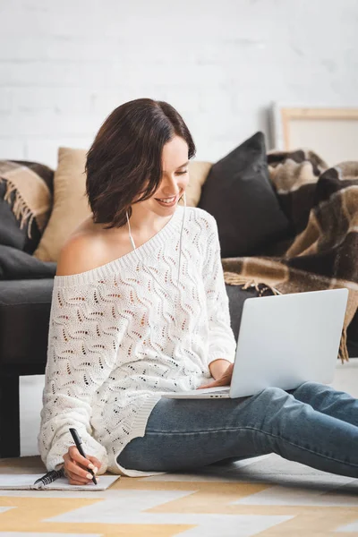 Glückliche junge Frau mit Kopfhörern, die zu Hause mit Laptop und Notebook online lernt — Stockfoto