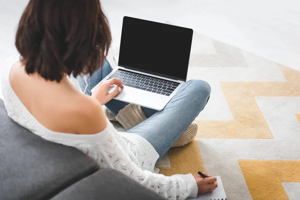 Vista posterior de la chica que estudia en línea con el ordenador portátil y la escritura en el cuaderno en casa - foto de stock