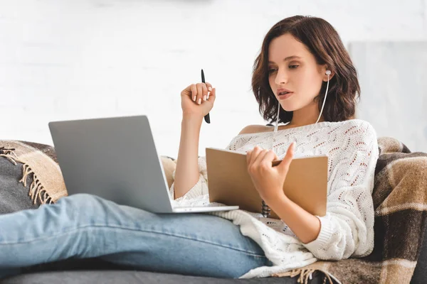 Привлекательная девушка учится онлайн с блокнотом, наушниками и ноутбуком — стоковое фото
