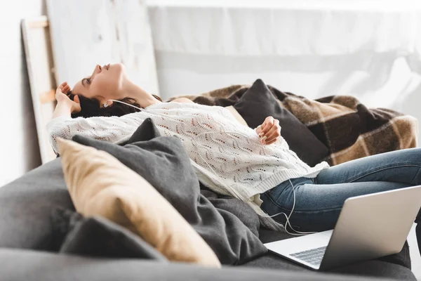 Menina cansada deitada no sofá com fones de ouvido e laptop — Fotografia de Stock