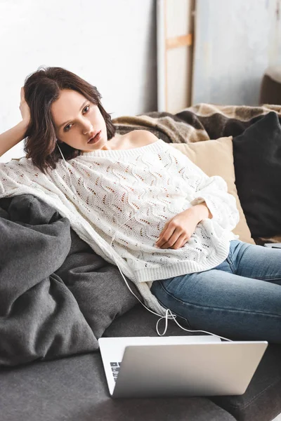 Verärgertes attraktives Mädchen sitzt mit Kopfhörern und Laptop auf Sofa — Stockfoto