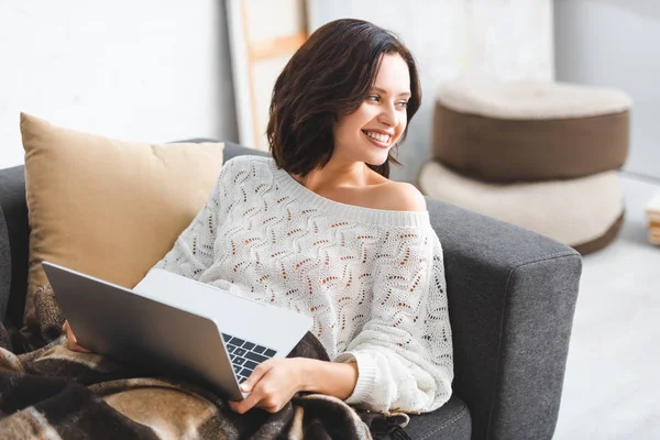 Bela menina feliz em cobertor usando laptop no sofá na acolhedora sala de estar — Fotografia de Stock