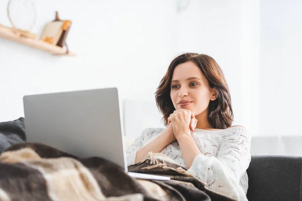 Happy young woman in blanket using laptop on sofa in cozy living room — Stock Photo