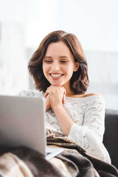 Attractive smiling girl in blanket using laptop on sofa in cozy living room — Stock Photo