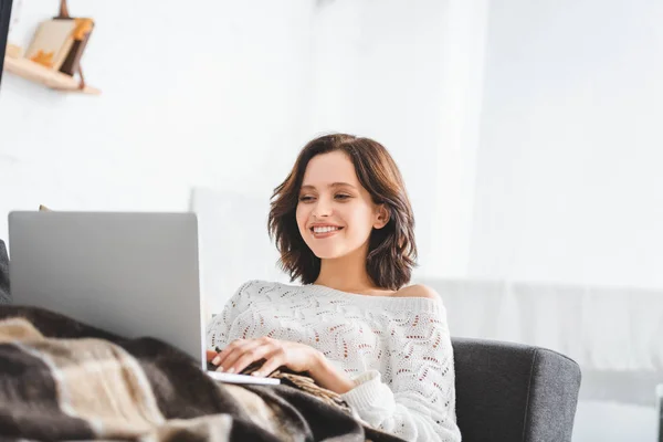 Hermosa mujer feliz en manta usando portátil en sofá en acogedora sala de estar — Stock Photo