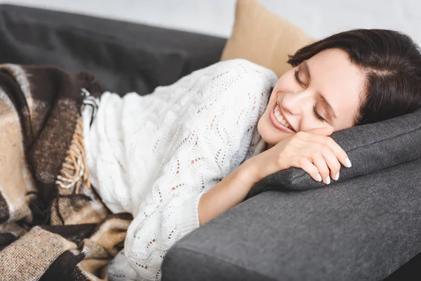 Glückliches schönes Mädchen mit geschlossenen Augen, das in einer Decke auf dem Sofa ruht — Stockfoto