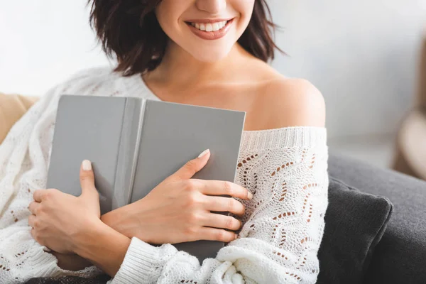 Vue recadrée de fille souriante tenant livre sur canapé à la maison — Photo de stock