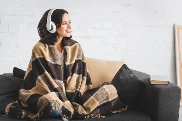 Brunette woman in blanket listening music with headphones — Stock Photo