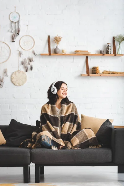 Брюнетка с закрытыми глазами в одеяле слушает музыку с наушниками — стоковое фото