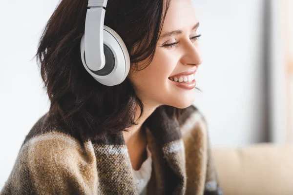 Mujer sonriente en manta escuchando música con auriculares - foto de stock