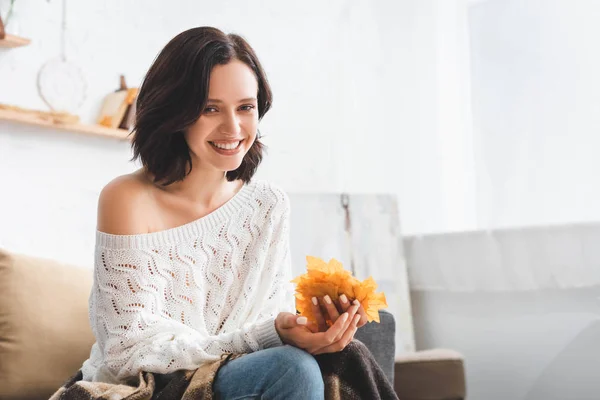 Hermosa mujer sonriente sosteniendo hojas de otoño amarillo en la sala de estar - foto de stock