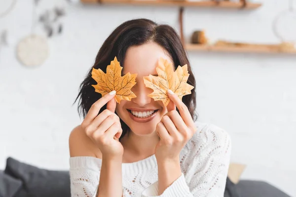Smiling girl holding yellow autumn leaves in front of eyes — Stock Photo