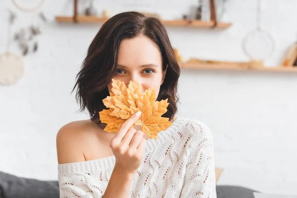 Beautiful woman holding yellow autumn leaves in front of face — Stock Photo