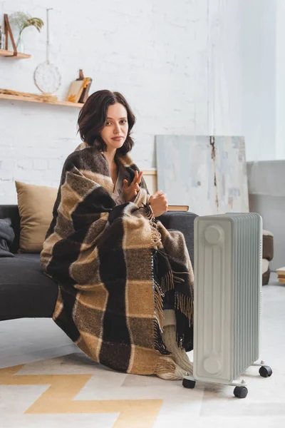 Beautiful cold woman with blanket warming up near heater — Stock Photo