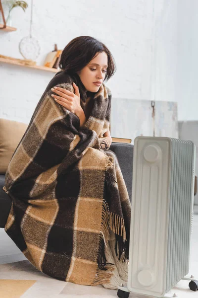 Beautiful cold girl with blanket in room with heater — Stock Photo
