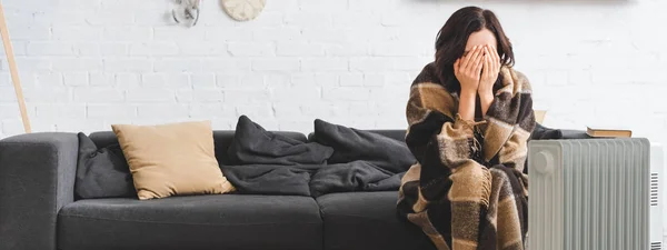 Menina bonita cobrindo seu rosto enquanto se aquece com cobertor e aquecedor na sala fria — Fotografia de Stock