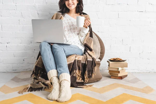 Обрезанный вид улыбающейся девушки с печеньем и кофе с помощью ноутбука — стоковое фото