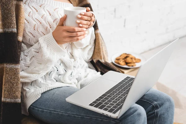 Cropped view of girl with cookies and coffee using laptop — Stock Photo