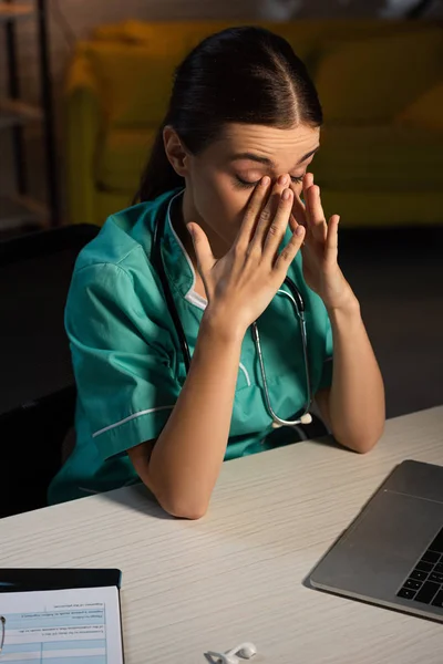 Приваблива і втомлена медсестра в уніформі сидить за столом під час нічної зміни — стокове фото