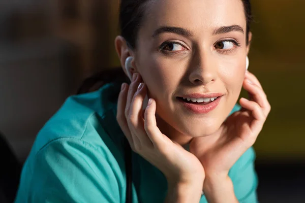 Attractive and smiling nurse in uniform listening music with earphones during night shift — Stock Photo