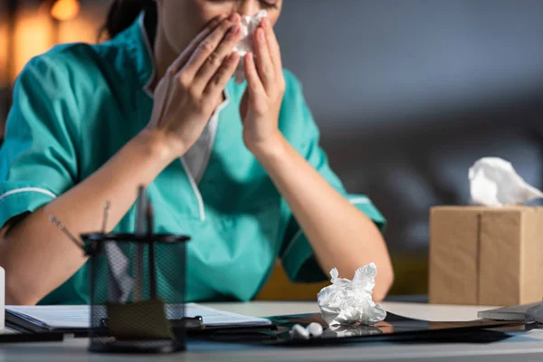 Cropped view of nurse in uniform sneezing and holding napkin during night shift — Stock Photo