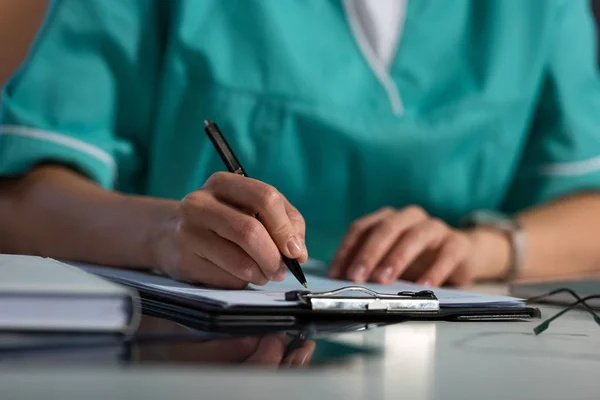 Vue recadrée de l'infirmière en uniforme écrivant dans le presse-papiers pendant le quart de nuit — Photo de stock