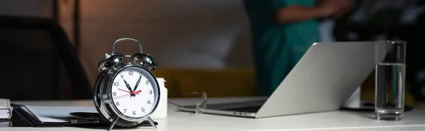 Tiro panorámico del reloj de alarma en la mesa de madera durante el turno de noche - foto de stock